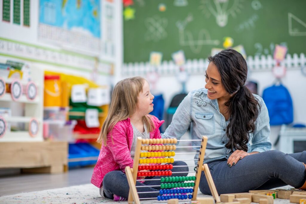 A child with SEND and a teacher sat smiling using an abacus