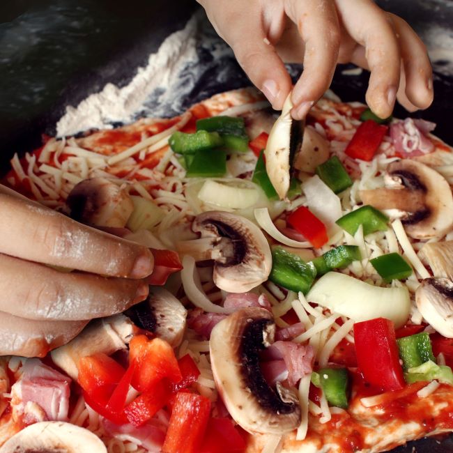 A close up of a child adding vegetables to a pizza topping