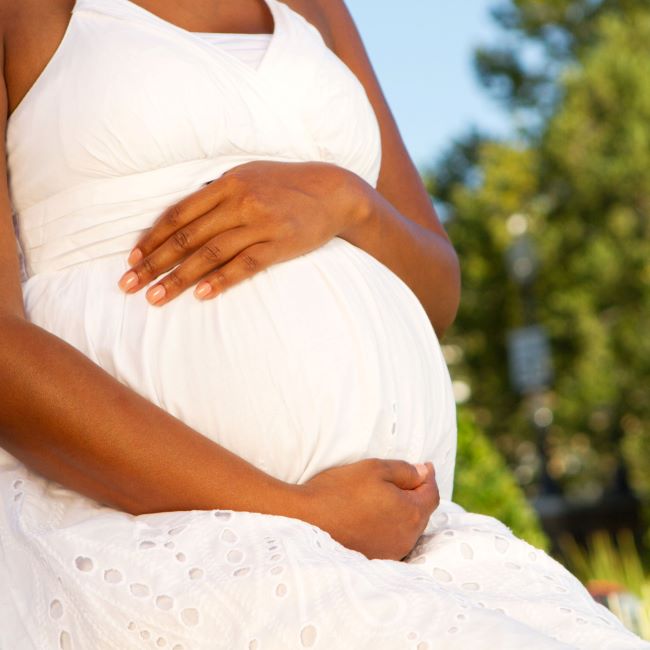 A woman cradles her pregnancy bump as she sits in the sun