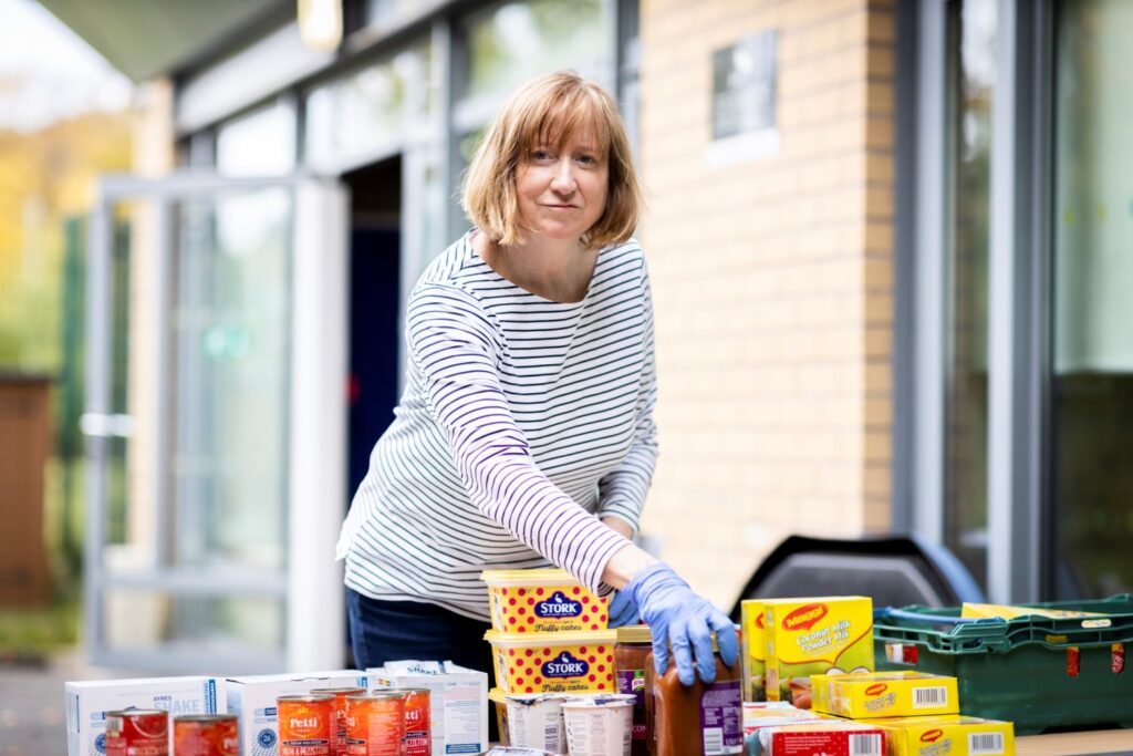 A female FOOD Club volunteer sets out packages of food on a table outside a centre