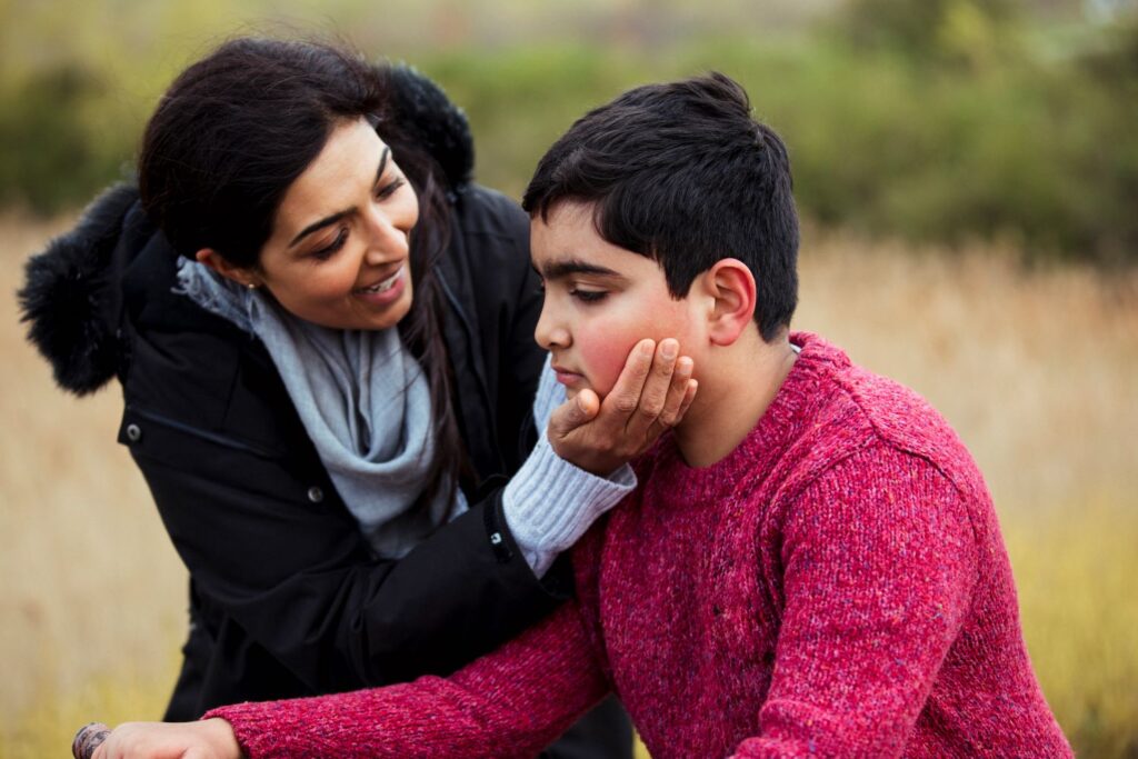 Young boy with SEND outdoors with a lady smiling and trying to encourage him to look at her