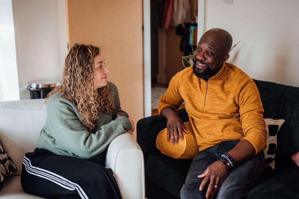 A man and a woman sit on separate sofas in the living room while they have a friendly chat.