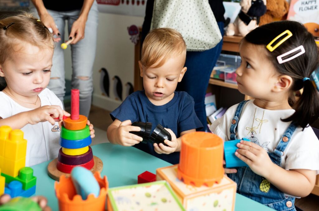 three pre-school children play with colourful stacking toys